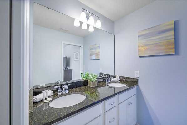 A bathroom with a large mirror, two sinks, a potted plant, and a painting on the wall. - Bengal Court Reserve (Kissimmee)