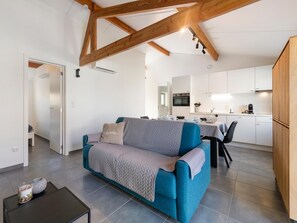 A modern living room with a sofa, a coffee table, and a kitchen in the background. - Cozy holiday home with a south-facing garden (Koksijde)