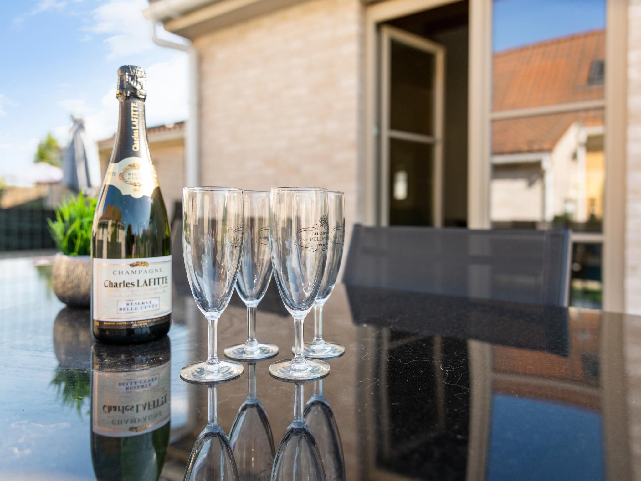 A bottle of Charles Lafitte champagne and four glasses on a reflective table.
