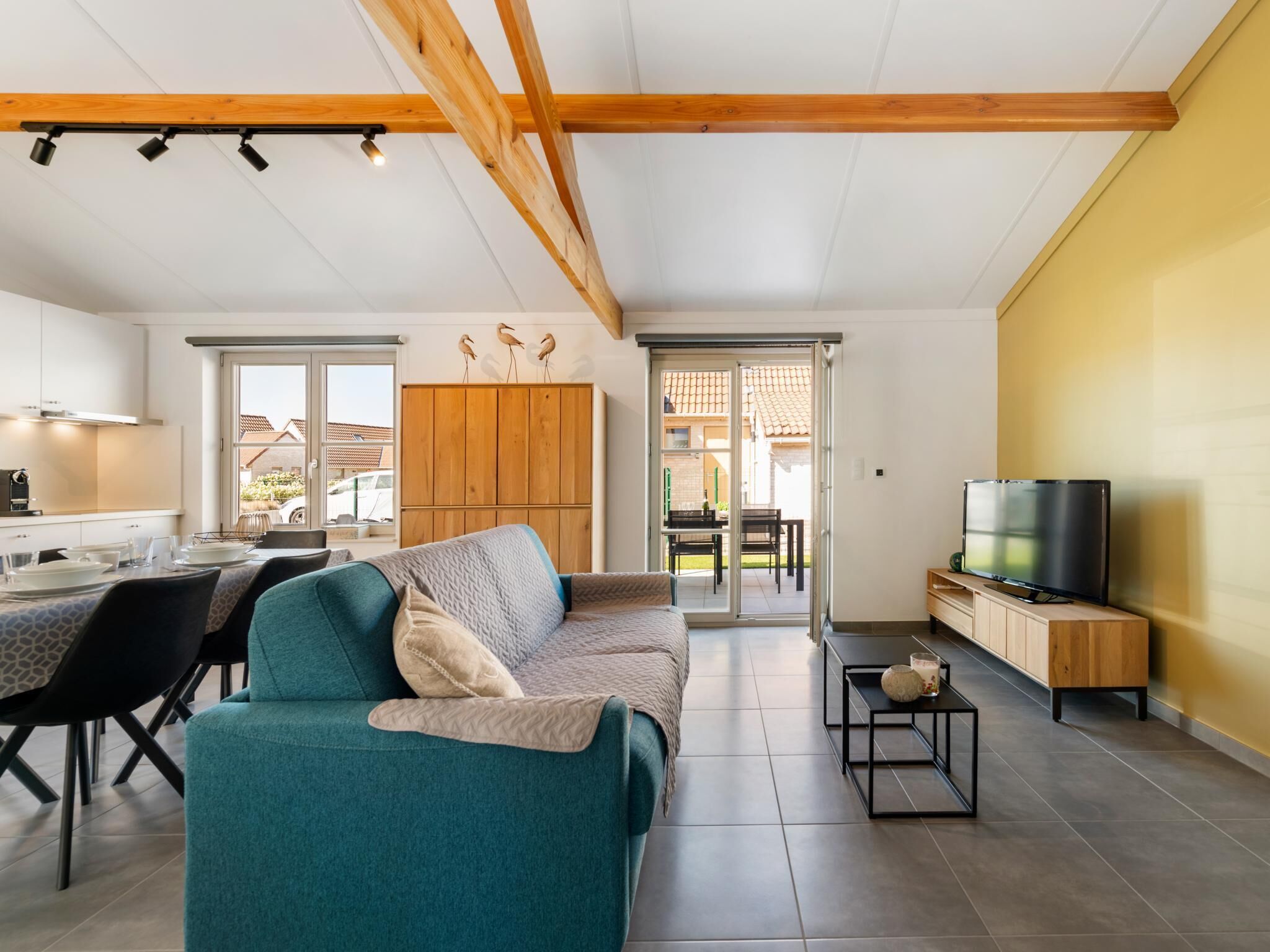 A modern living room with a sofa, a dining area with chairs, a kitchen with cabinets, and a TV on a stand.