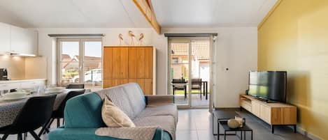 A modern living room with a sofa, a dining area with chairs, a kitchen with cabinets, and a TV on a stand.