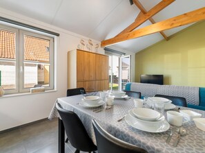 A dining area with a table set for four, a wooden cabinet, and a television on a wall. - Cozy holiday home with a south-facing garden (Koksijde)