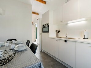 A modern kitchen with white cabinetry, a built-in oven, and a dining area with a table set for four. - Cozy holiday home with a south-facing garden (Koksijde)