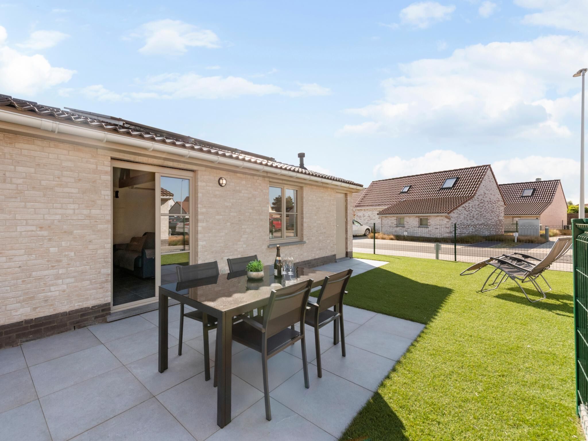 A patio with a table and chairs, a lawn, and a brick building with a tiled roof.