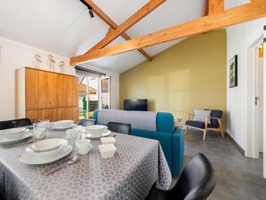 A dining area with a table set for four, a sofa, and a television in the background. - Cozy holiday home with a south-facing garden (Koksijde)
