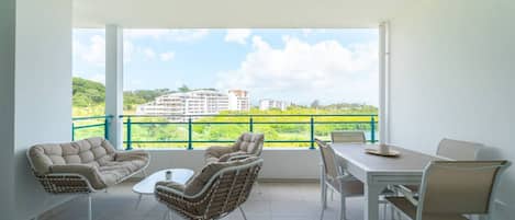 A balcony with a dining table and chairs, a sofa, and a view of greenery and buildings.