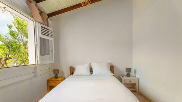 A bedroom with a single bed, two bedside tables, a window with a view of greenery, and a sloped ceiling.
