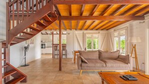 A spacious living area with a wooden staircase, a sofa, a coffee table, and a fan.