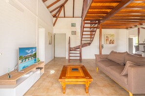 A living room with a wooden coffee table, a sofa, a TV on a stand, and a staircase leading to another room.