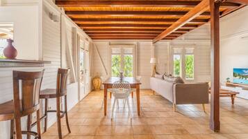 Amplia habitación con techo de madera, zona de comedor con mesa y sillas, sofá y televisor.