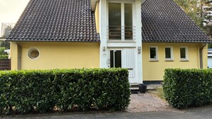 Et hus i to etager med et tegltag, en lille balkon og en dør med et vindue.