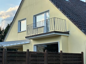 A two-story house with a balcony, a wooden fence, and a tiled roof.
