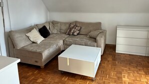 En moderne stue med en krogsofa, et hvidt opbevaringsskab og et parketgulv.