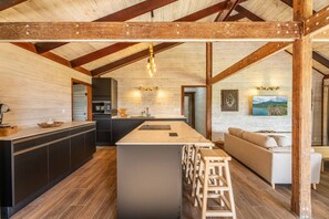 A modern kitchen with a central island, dark cabinetry, and a wooden ceiling structure.
