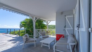 A covered outdoor seating area with a view of the ocean, featuring a table and two chairs.