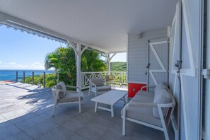 A covered outdoor seating area with a view of the ocean, featuring a table and two chairs.