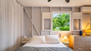 A bedroom with a bed, bedside tables, a dresser, and a window with a view of greenery.