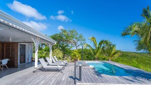 A wooden deck with a pool, lounge chairs, and a covered area with a pergola.