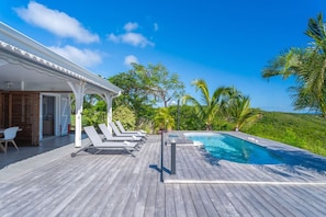 A wooden deck with a pool, lounge chairs, and a covered area with a pergola.