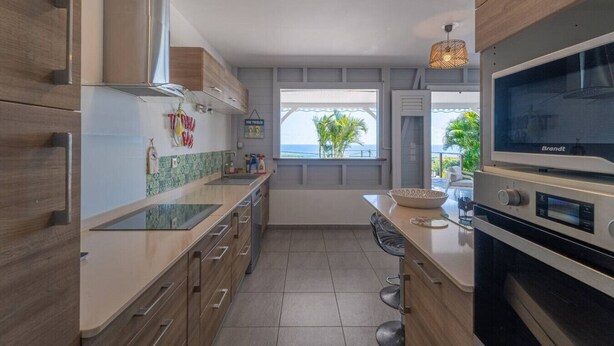 A modern kitchen with a large island, stainless steel appliances, and a view of the sea.