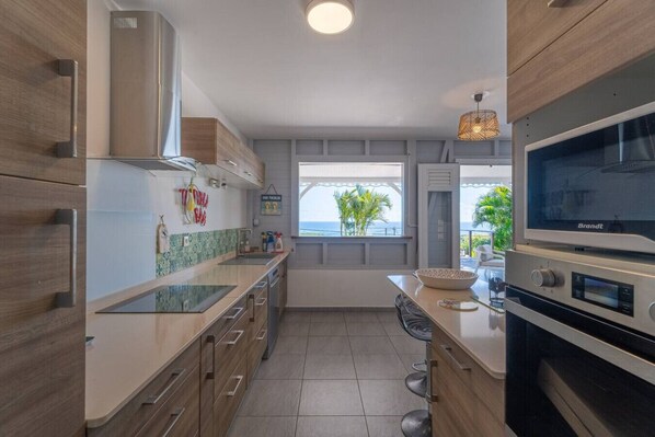 A modern kitchen with a large island, stainless steel appliances, and a view of the sea.