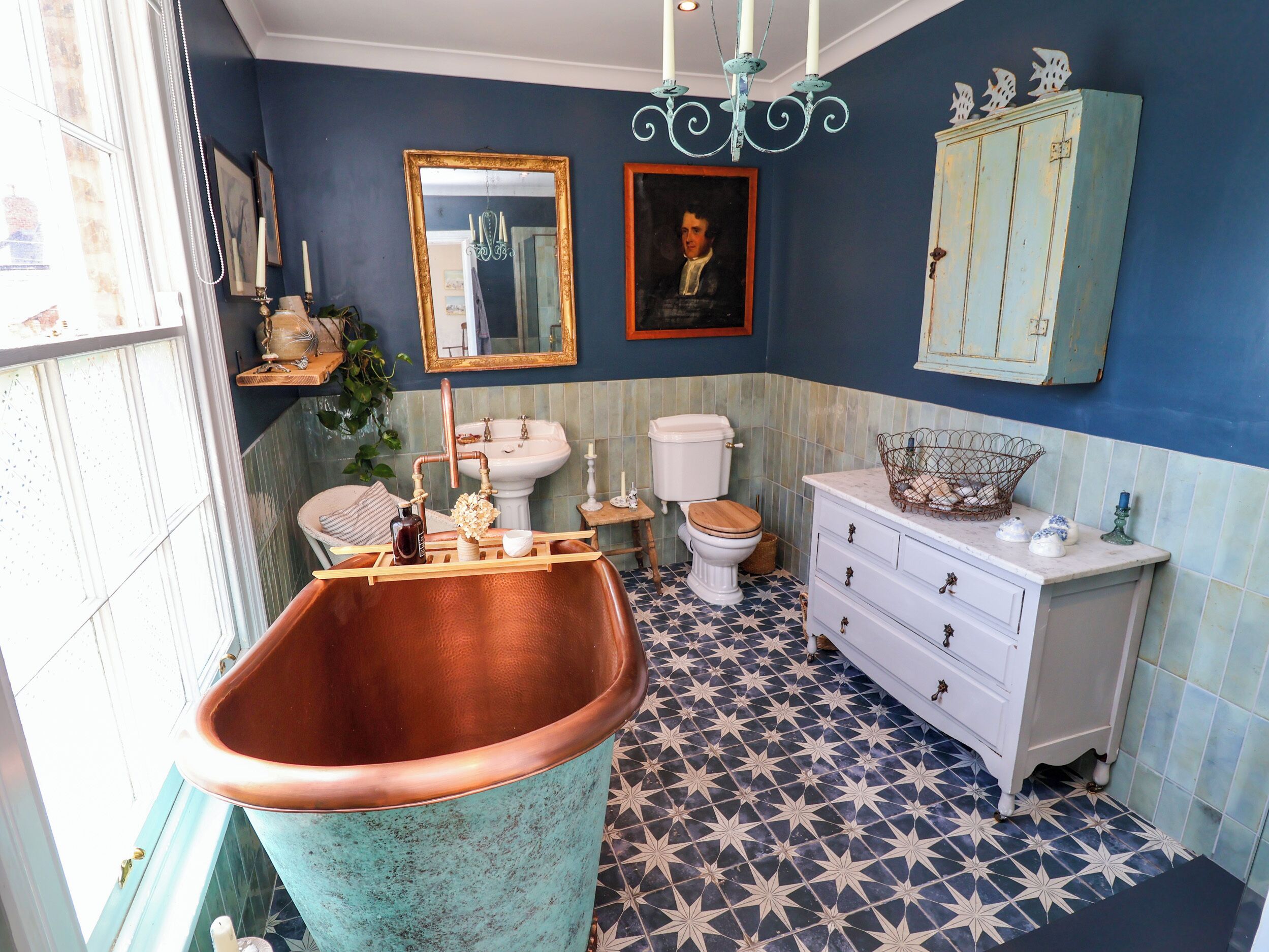 A bathroom with a large copper bathtub, a white sink, a toilet, and a vintage cabinet.