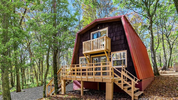 Une cabane dotée d’une terrasse en bois et d’un toit rouge, entourée d’arbres.