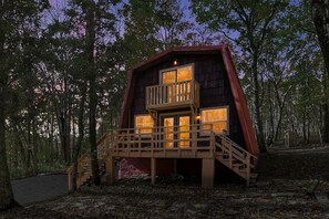 Una cabaña con balcón y una escalera que lleva a él, rodeada de árboles.