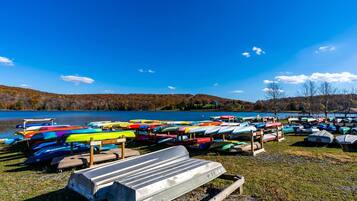 A lakeside view with a row of colorful kayaks and a wooden bench.