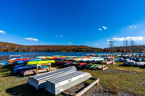 Vista lacustre con una hilera de kayaks de colores y un banco de madera.