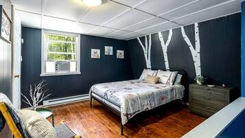 A bedroom with a bed, dresser, chair, and artwork on the wall.