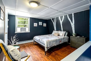 Un dormitorio con cama, cómoda, silla y una obra de arte en la pared.