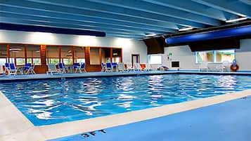 An indoor swimming pool with blue water, marked lanes, and blue chairs along the side.