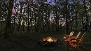 Um camping com uma fogueira e duas cadeiras de madeira.