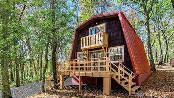 Una cabaña con terraza de madera y techo rojo, rodeada de árboles.