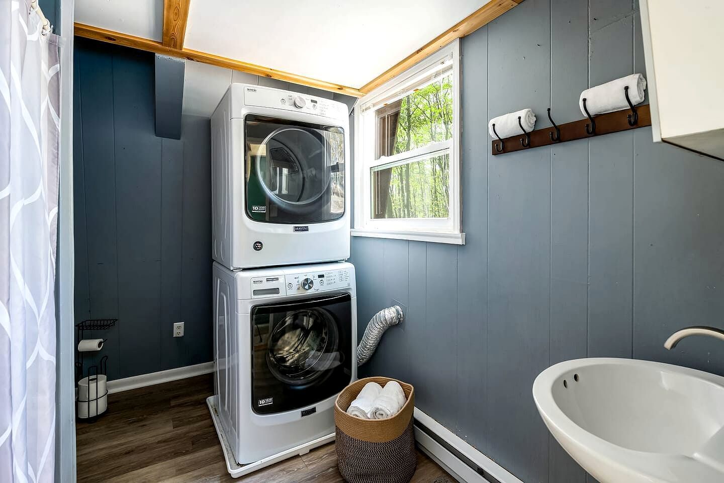 A laundry room with stacked washing machines, a window, a towel rack, and a bathtub.