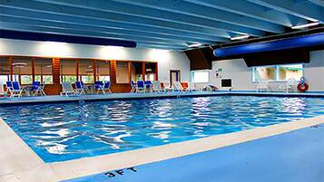 Una piscina interior con agua azul, carriles delimitados y sillas azules a lo largo del borde.