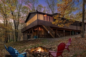 Uma cabana com lareira, duas cadeiras Adirondack e um deck com vista para uma floresta.