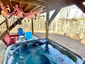 A hot tub with a wooden deck, surrounded by chairs and a view of a wooded area. - Awesome Wooden Cabin with Fire Pit in Great Cacapon, West Virginia (Great Cacapon)