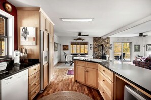 A modern kitchen with wooden cabinets, a central island, and a stone accent wall. - Awesome Wooden Cabin with Fire Pit in Great Cacapon, West Virginia (Great Cacapon)