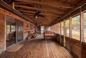 Uma cabana de madeira com varanda, ventilador de teto e vista para a folhagem outonal.