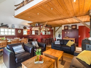 A spacious room with wooden ceiling beams, leather sofas, a wooden coffee table, and a bar area with bottles. - Charming farm with sauna and hot tub (Balkbrug)