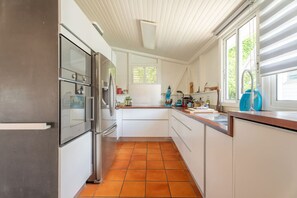 A kitchen with white cabinets, a stainless steel refrigerator, a blue mixer, and a window with blinds. - Villa Blue Rock, Pool & Stunning View (Rivière-Salée)