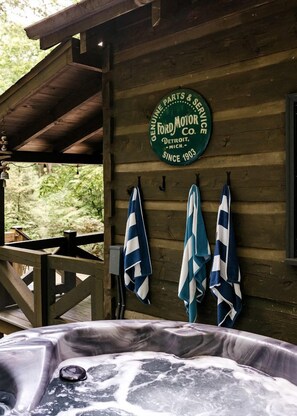 A wooden cabin with a hot tub, towels hanging on a wall, and a sign indicating it's a genuine parts and service center for Ford Motor Co. since 1903. - Enchanting Creekside Mountain Cabin Retreat with Luxury Amenities in the Heart of Scenic Blue Ridge, Georgia (Blue Ridge)
