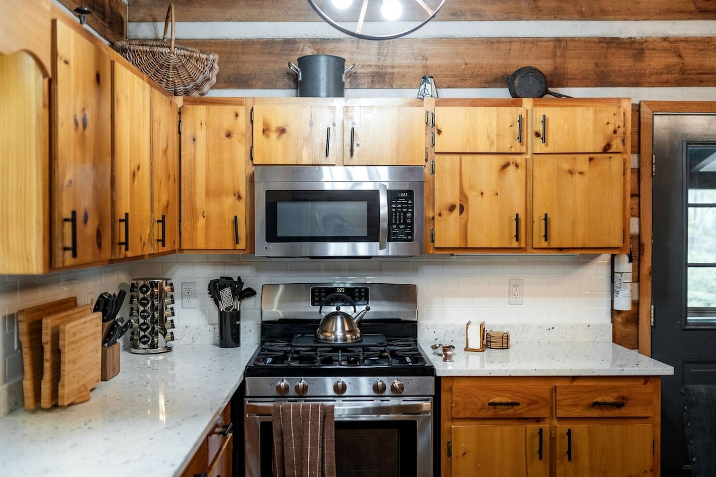 A kitchen with wooden cabinets, a stainless steel microwave, a gas stove, and a kettle.