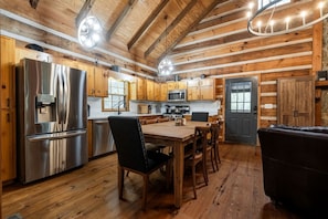 A modern kitchen with wooden cabinets, stainless steel appliances, and a dining area with a black leather couch. - Enchanting Creekside Mountain Cabin Retreat with Luxury Amenities in the Heart of Scenic Blue Ridge, Georgia (Blue Ridge)