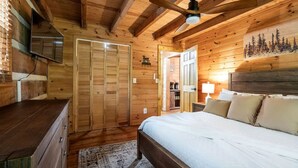 Ein Schlafzimmer einer Holzhütte mit Bett, Kommode, Kleiderschrank und Deckenventilator.