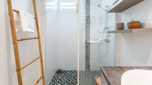Moderni kylpyhuone, jossa on lasinen suihkuseinä, puinen tikapuu ja laatoitettu lattia.