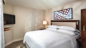 Ein Hotelzimmer mit einem Bett, einem an der Wand befestigten Fernseher, einer Lampe und einem Gemälde.