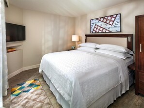 A hotel room with a bed, a TV mounted on the wall, a lamp, and a painting. - Family-Friendly 2 Bedroom Villa at Kaua'i Resort (Koloa)